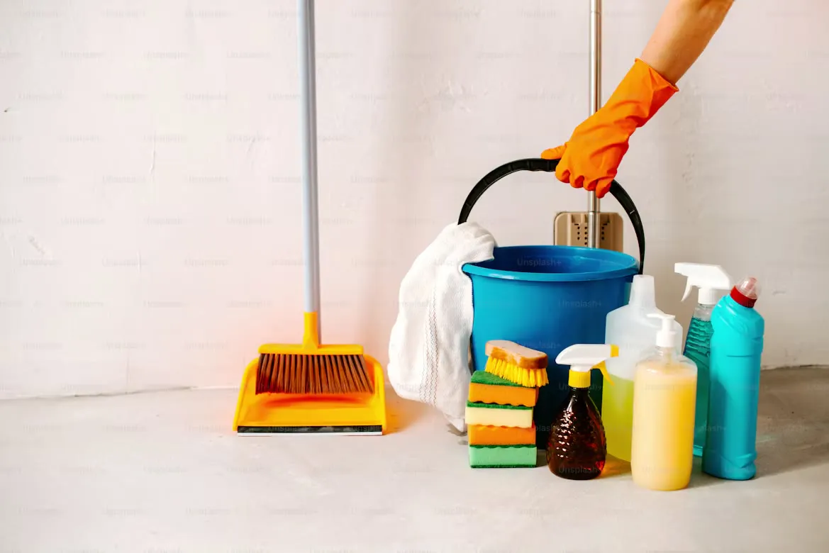 A cleaner wiping a worktop with supplies to hand